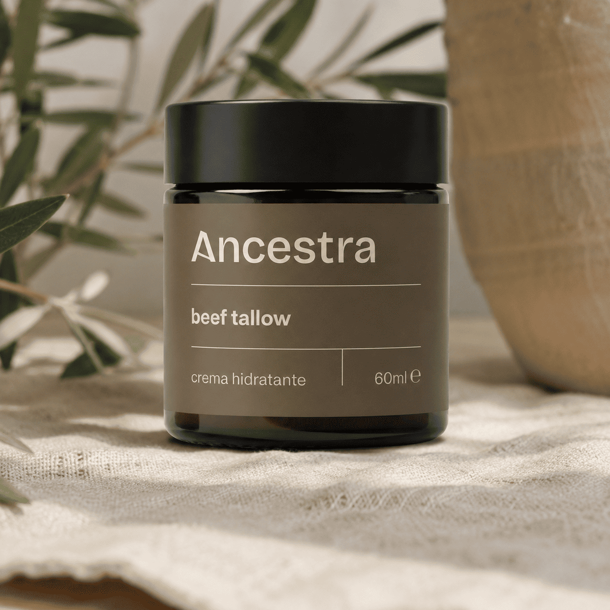 Crema hidratante de beef tallow de Ancestra sobre lino junto a una rama de olivo